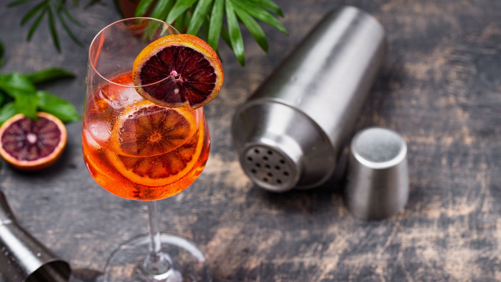 Oranger Cocktail mit Eiswürfeln und Obstgarnitur.